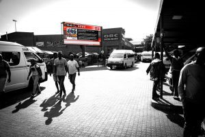 Commuters at a taxi rank viewing large format digital screen